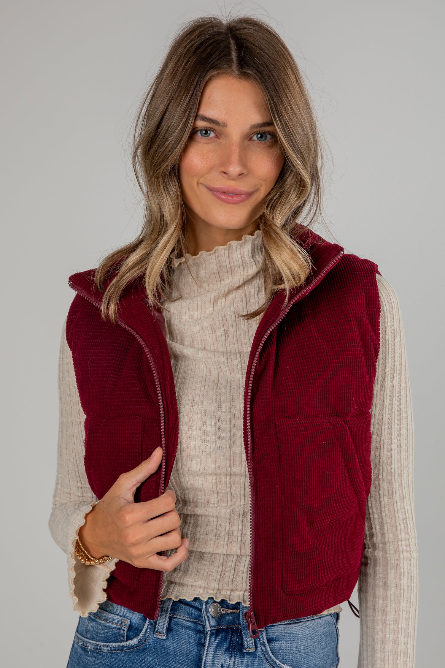 Woman wearing a red vest over a beige sweater with a gray background