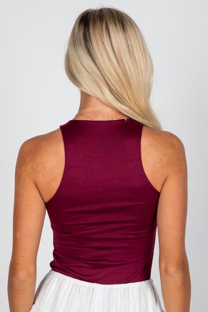 Person wearing a burgundy sleeveless top with a plain background