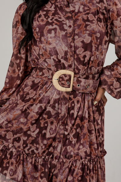 A close-up of a long-sleeve button-front dress with an abstract animal-like print in dusty mauve, brown, and burgundy tones, featuring a matching waist belt with a large round natural-fiber buckle.