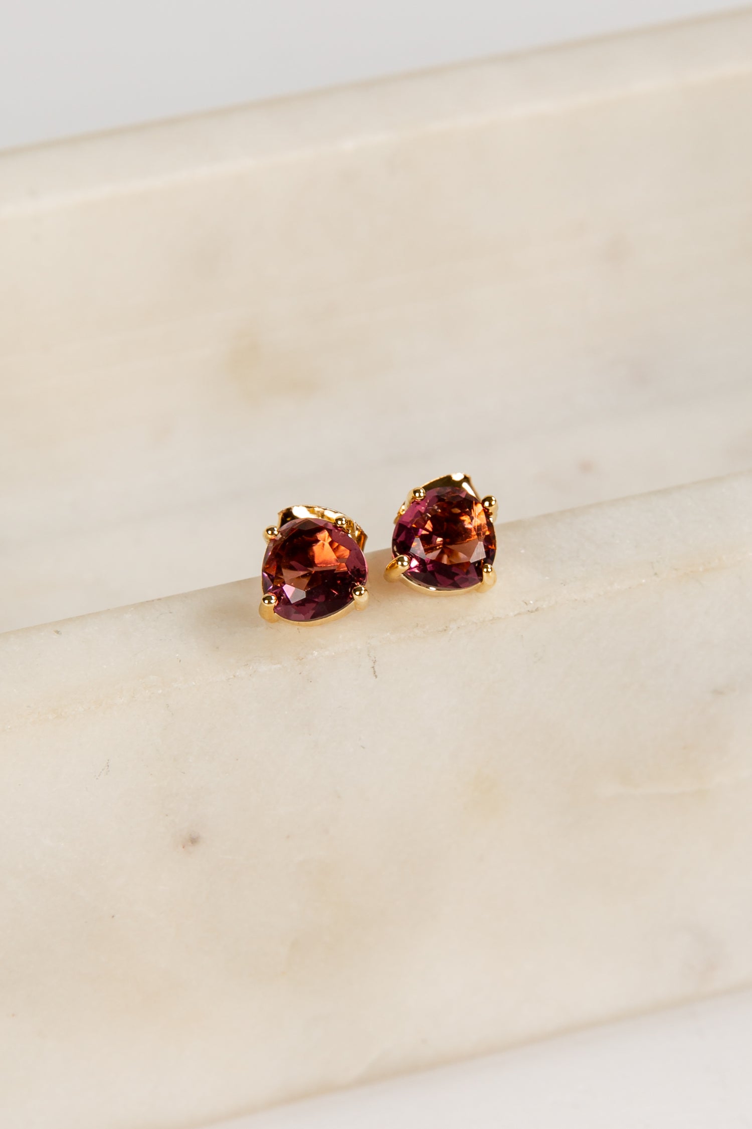 Pair of red gemstone stud earrings on a light beige surface