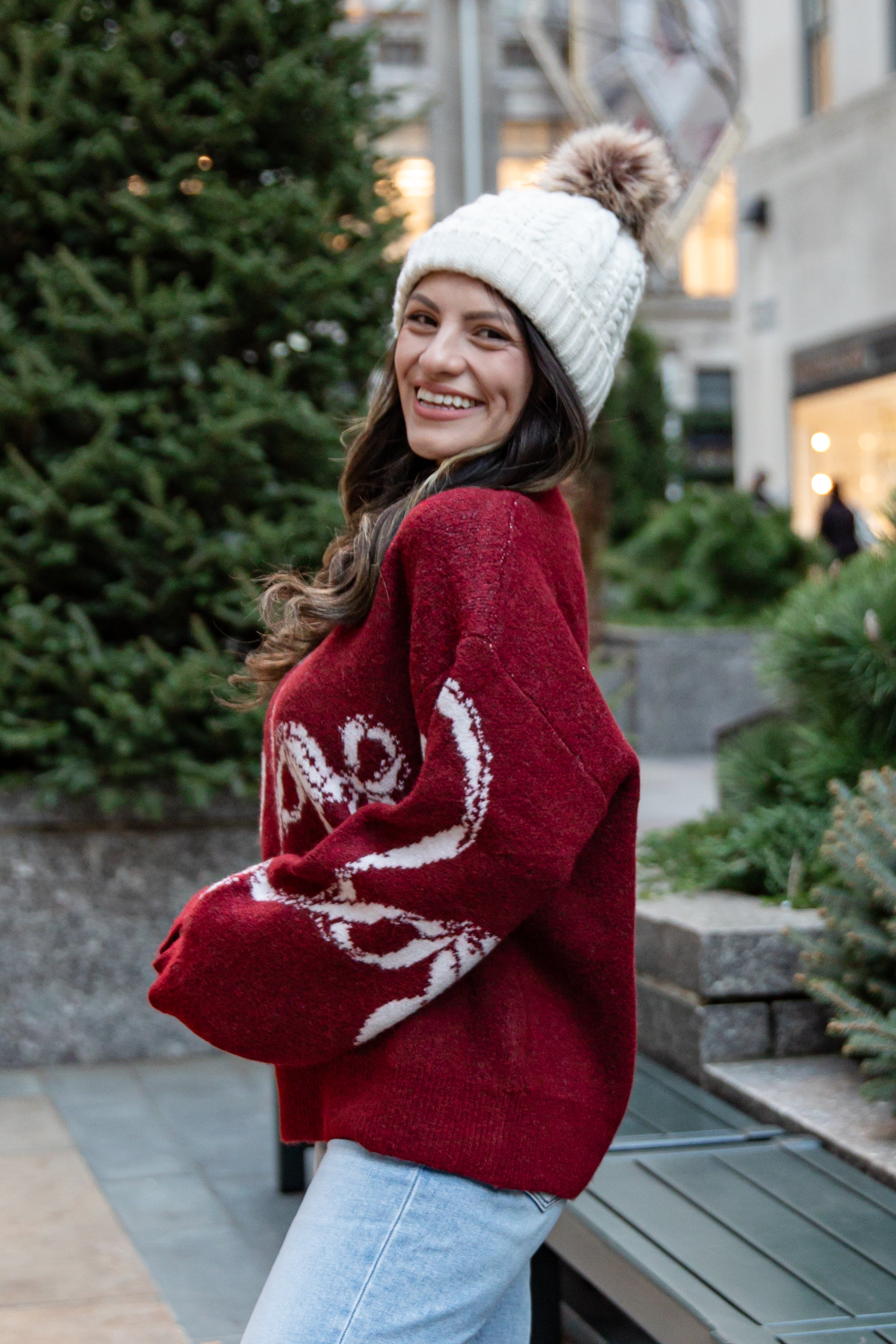 Woman wearing a red sweater with white designs and a white beanie outdoors.