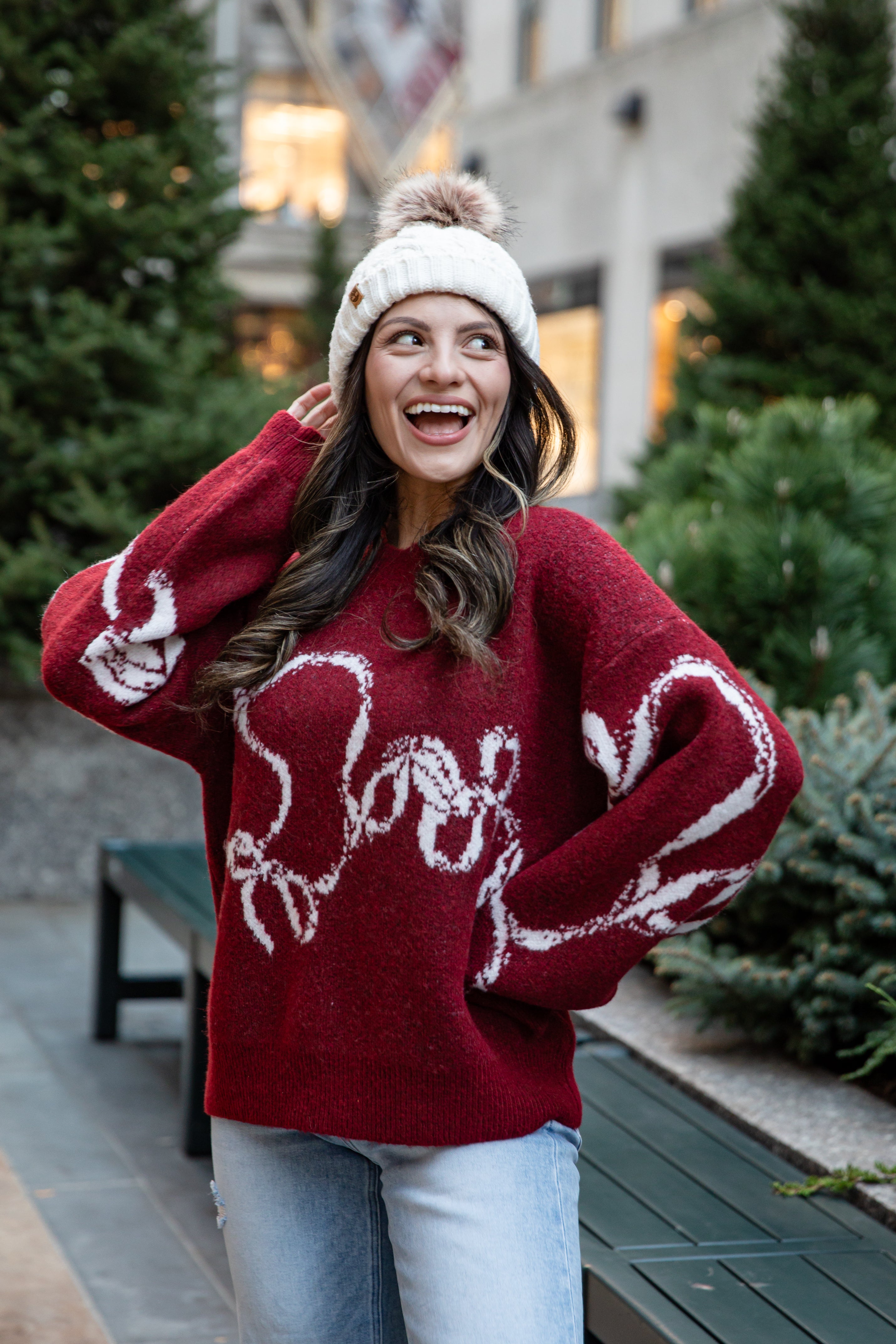Woman wearing a red sweater with white text, standing outdoors in a festive setting.