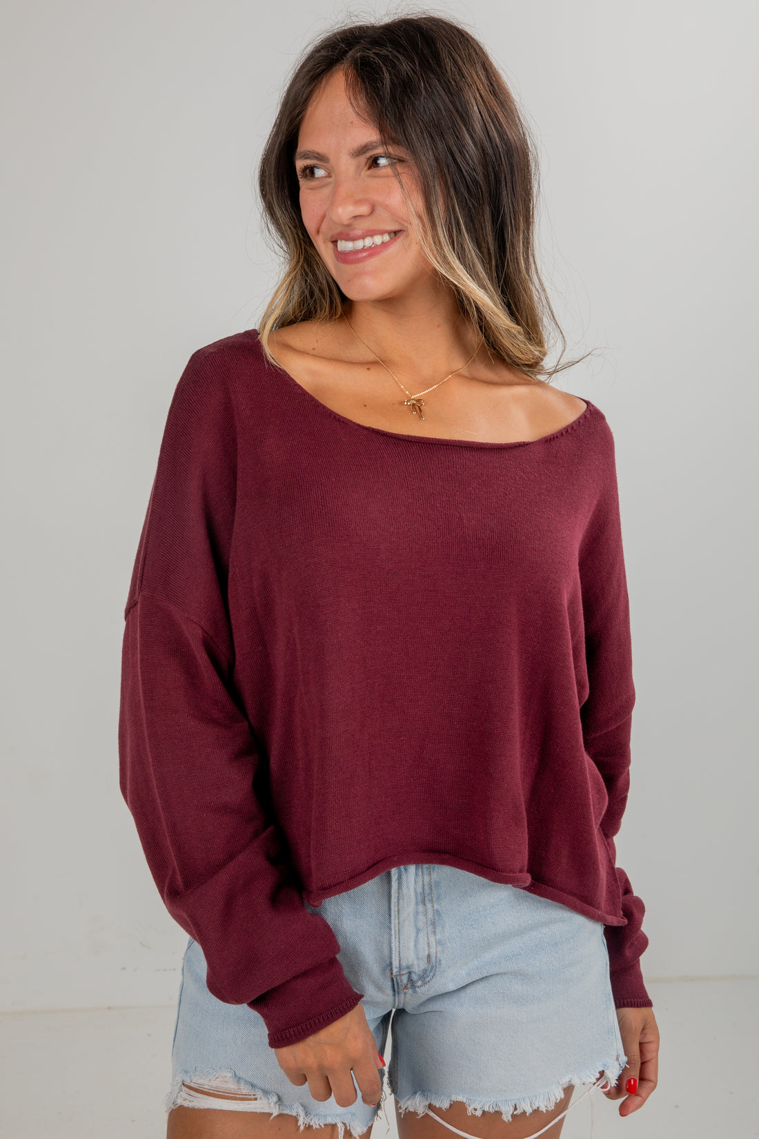 Woman wearing a burgundy sweater and denim shorts on a plain background