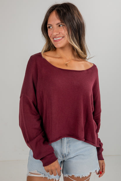 Woman wearing a burgundy sweater and denim shorts on a plain background