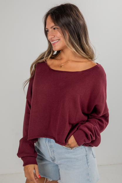 Woman wearing a burgundy sweater and light blue jeans against a plain background