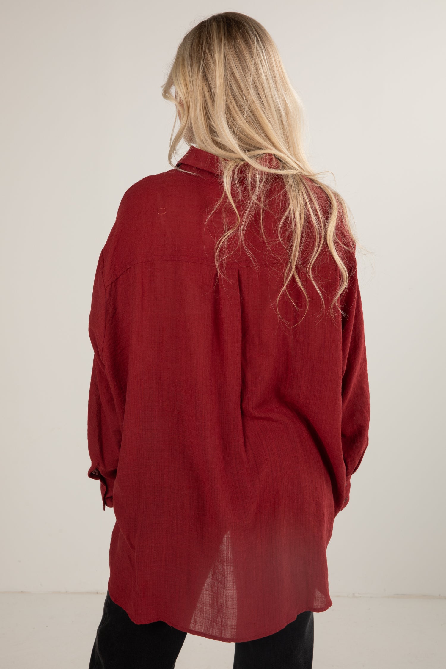 Person wearing a red shirt with long sleeves and a high collar, standing against a plain background.