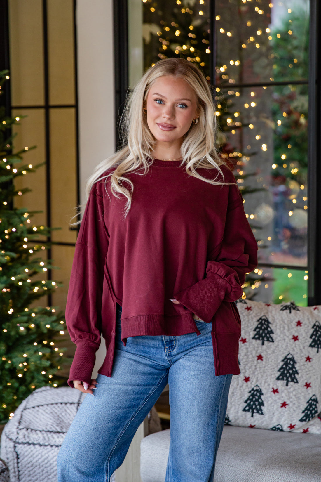Woman wearing a burgundy sweater and blue jeans standing in a festive living room.