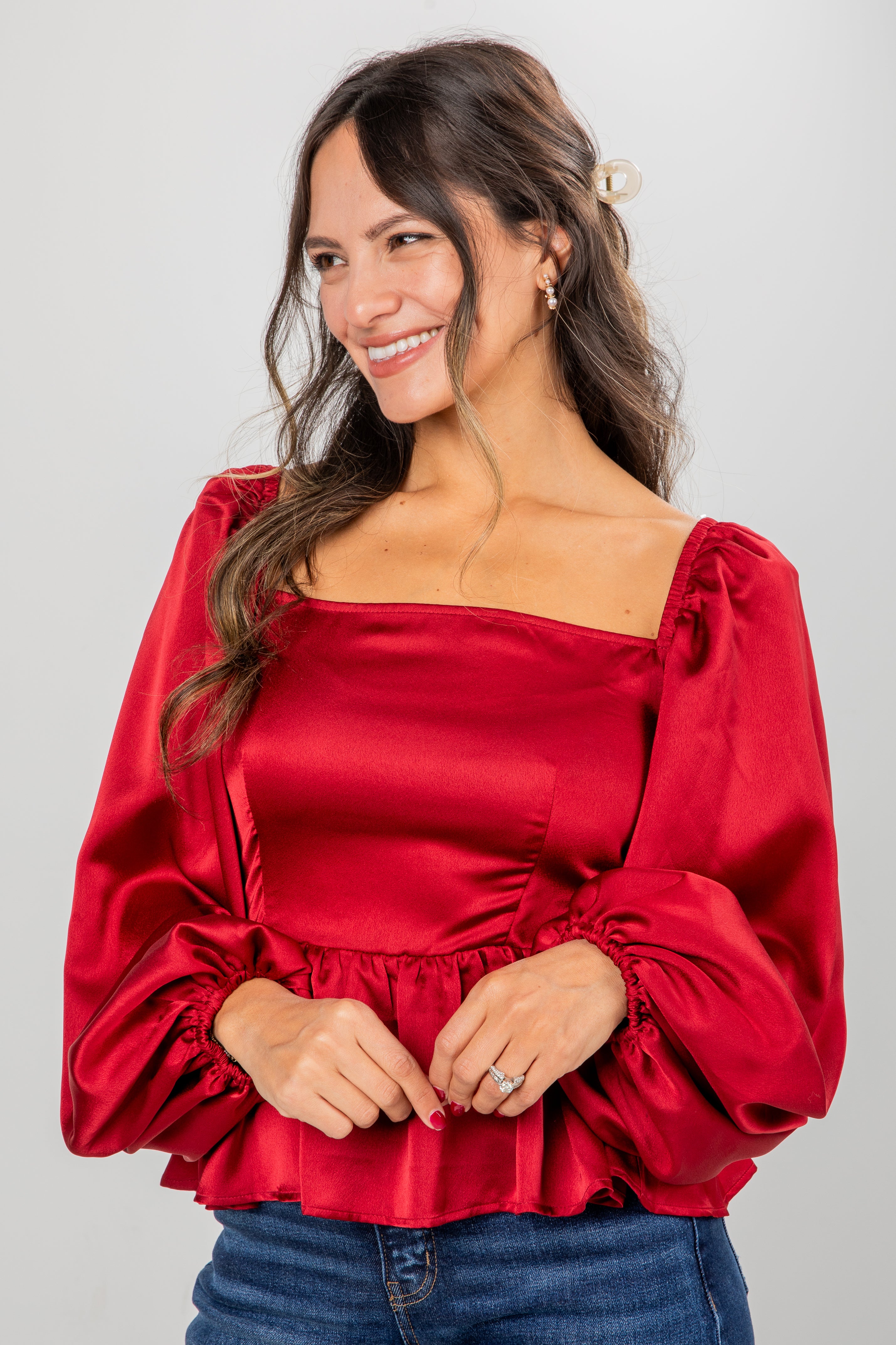 Woman wearing a red satin blouse with puffed sleeves against a gray background