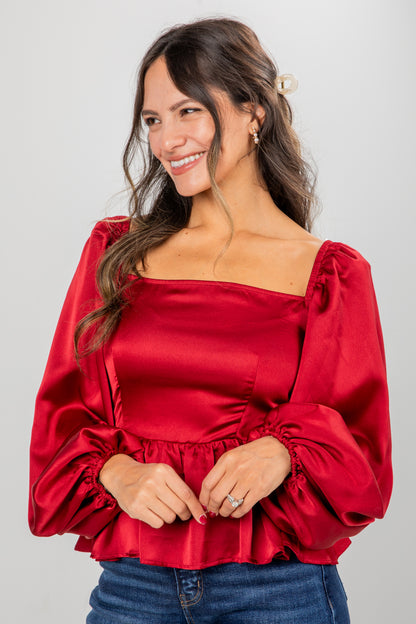 Woman wearing a red satin blouse with puffed sleeves against a gray background