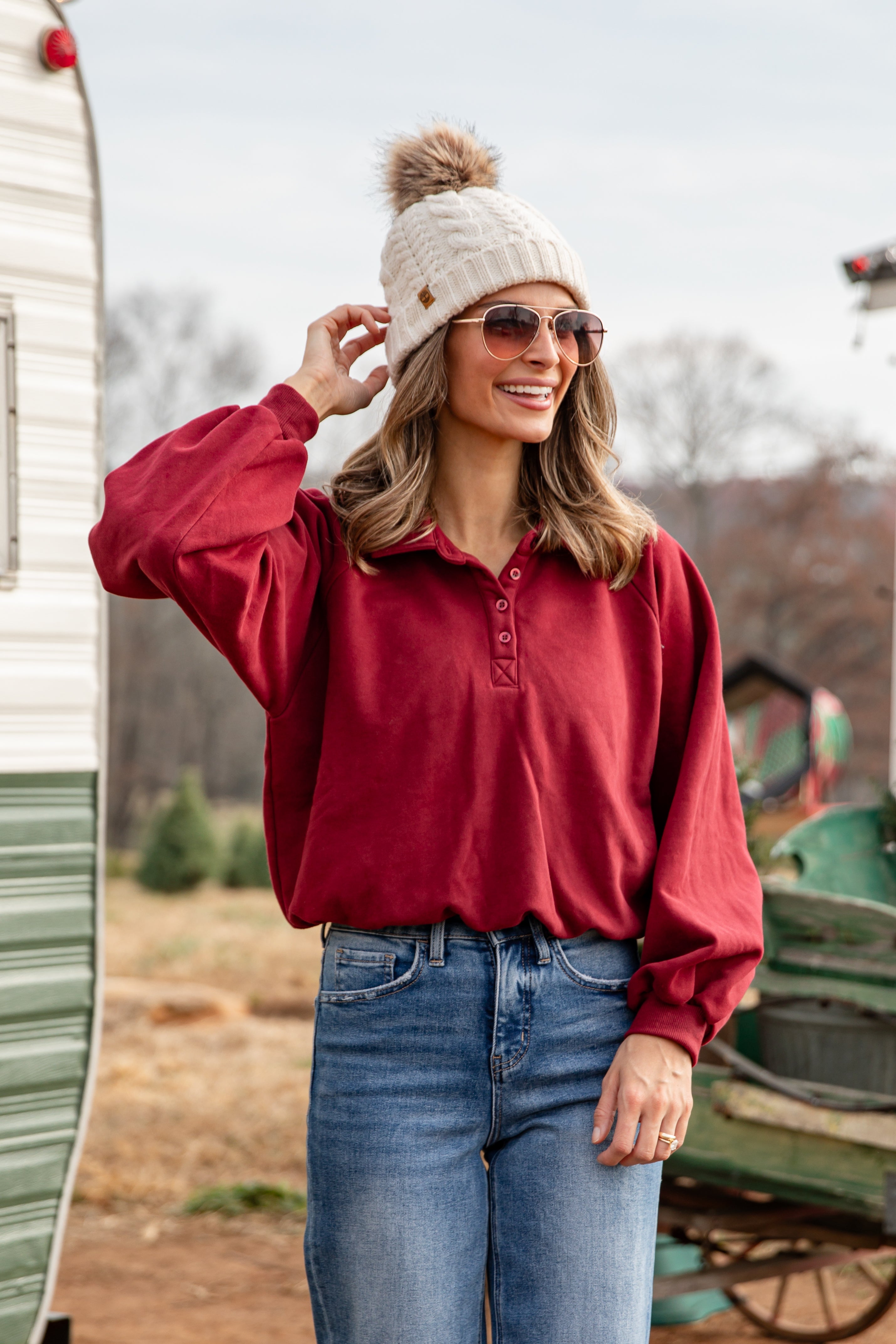 Woman wearing a red shirt, white beanie, and sunglasses outdoors.