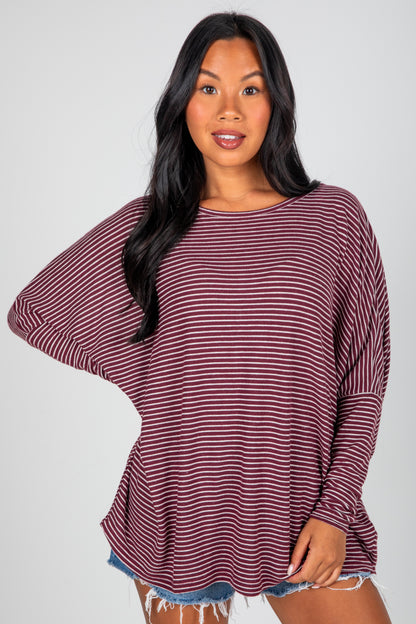 Woman wearing a maroon and white striped long-sleeve top on a gray background