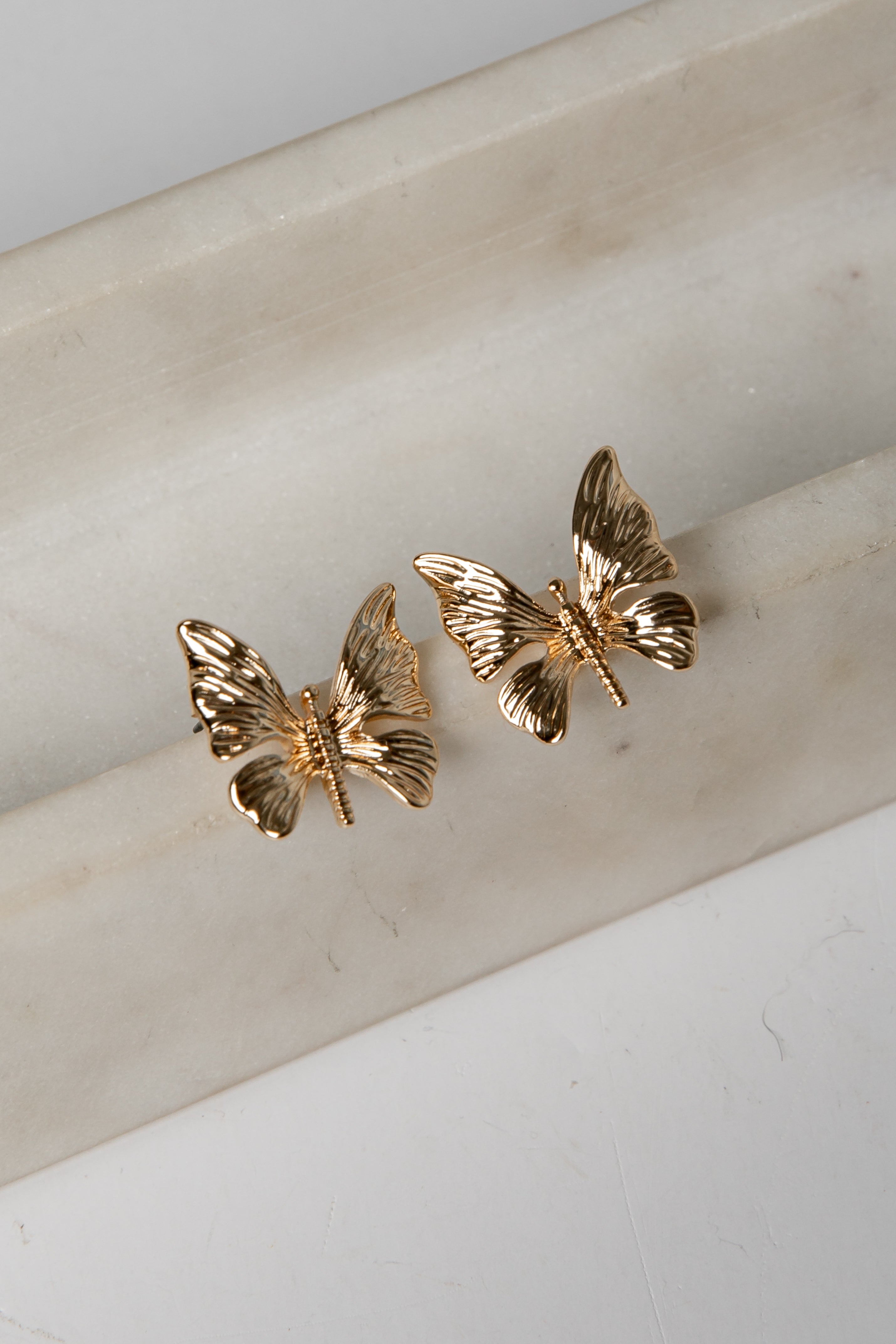 Gold butterfly earrings on a marble surface