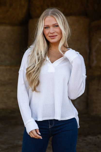 Woman wearing a white blouse and blue jeans standing in front of hay bales.