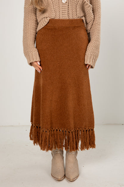 Person wearing a brown knitted skirt with fringe on a white background