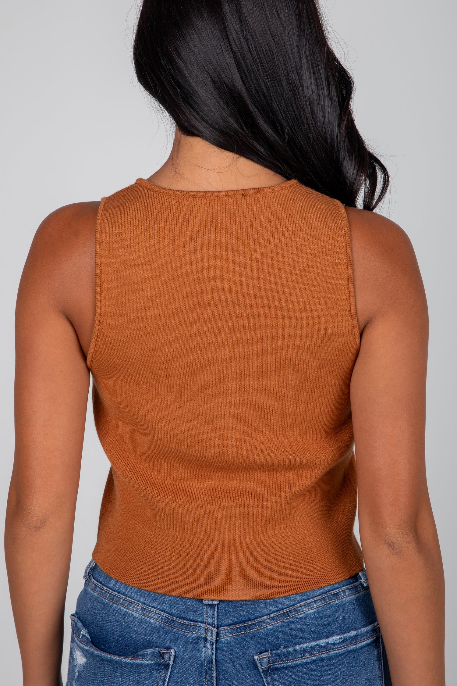 Person wearing a brown sleeveless top and blue jeans on a plain background