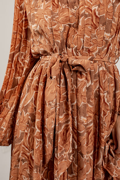 A close-up of a long-sleeve dress with a brown and beige paisley pattern, featuring a matching fabric tie belt at the waist.