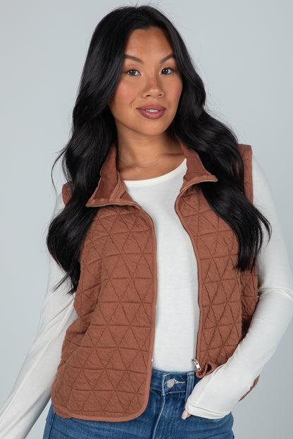 Woman wearing a brown quilted vest over a white shirt with a gray background