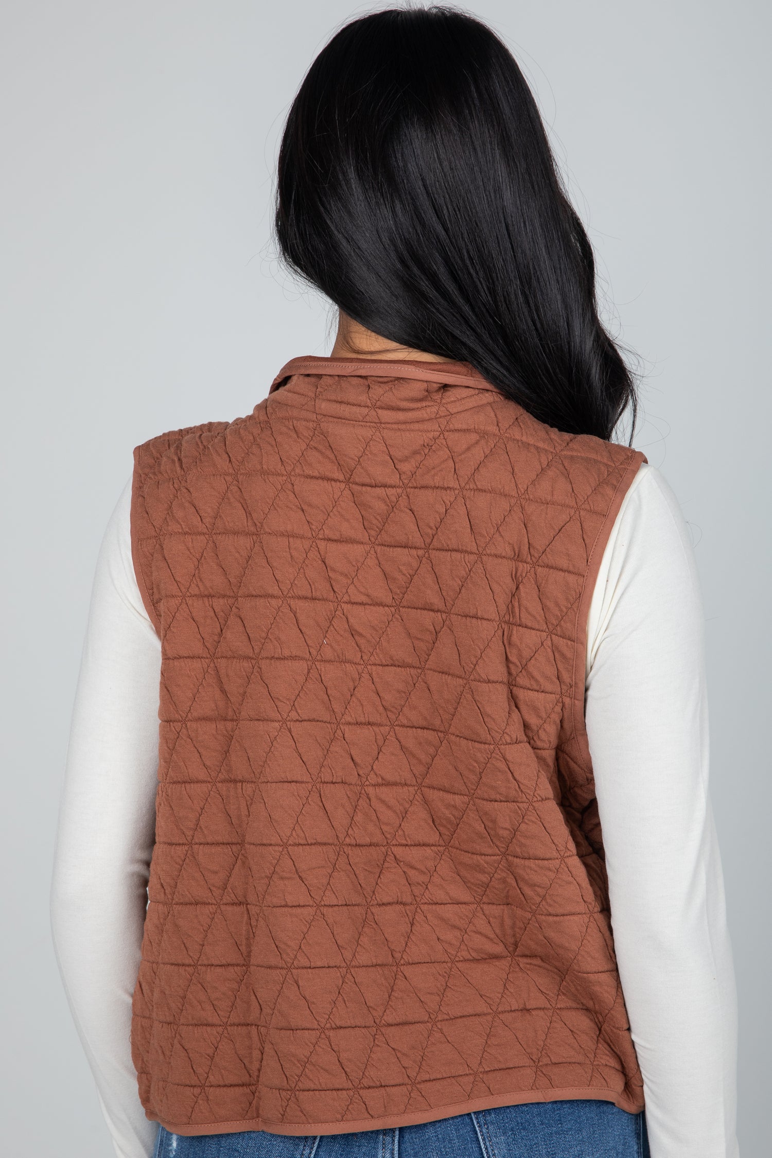 Person wearing a brown quilted vest on a plain background