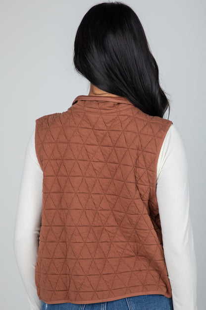 Person wearing a brown quilted vest on a plain background