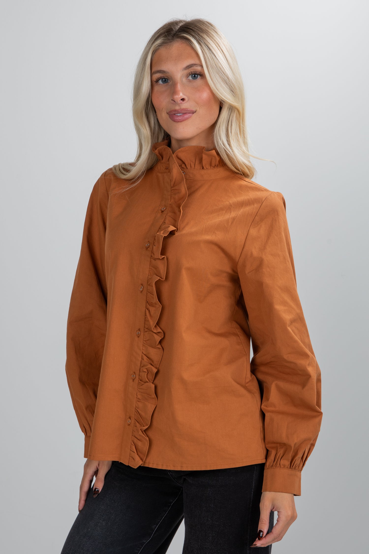 Woman wearing a brown blouse with ruffled details on a plain background