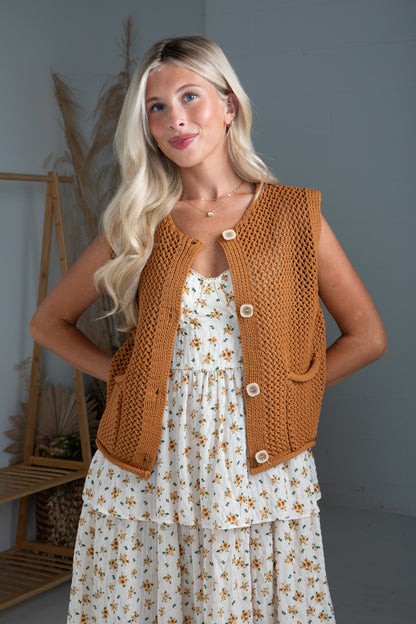 Woman wearing a brown knitted vest over a floral dress indoors.