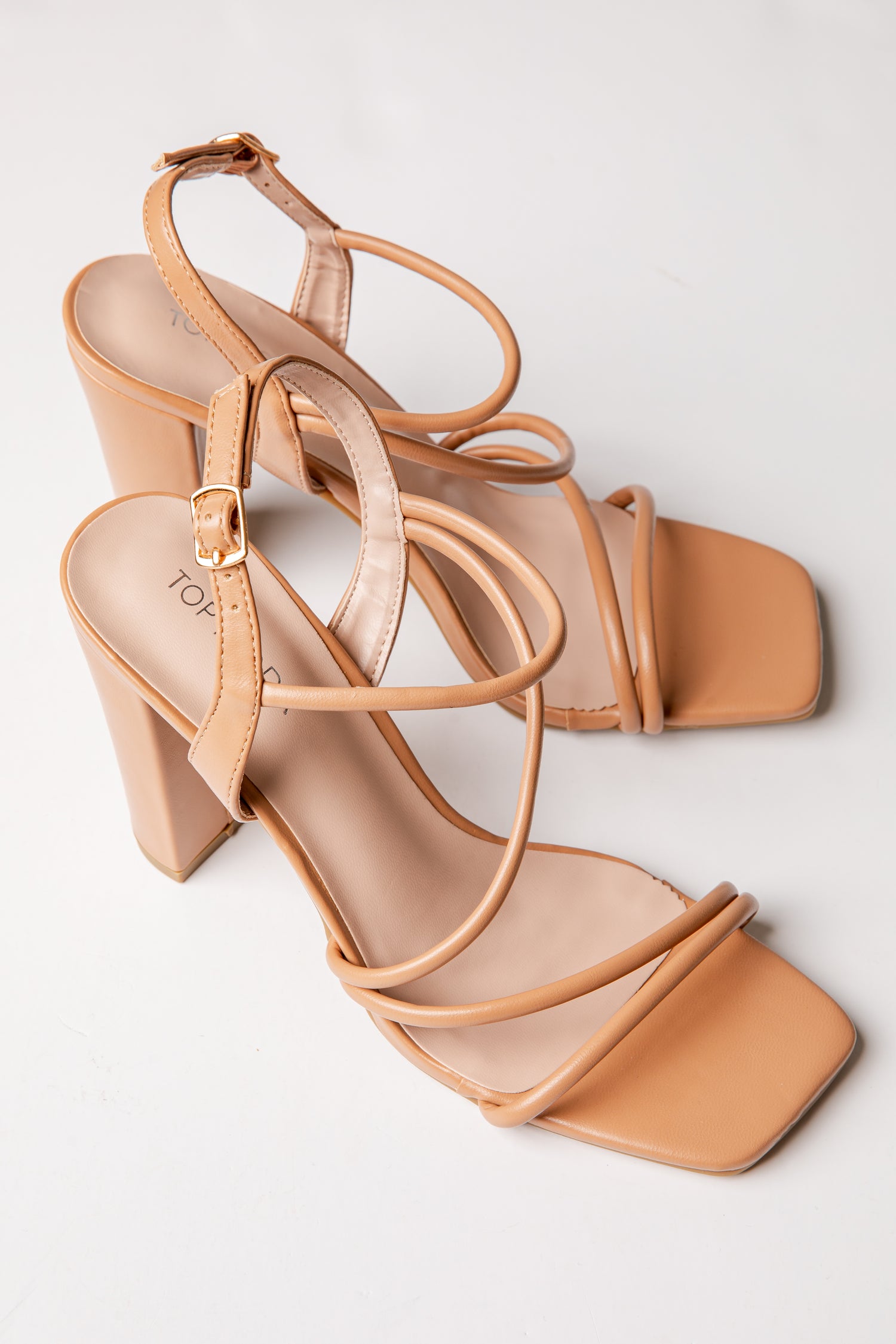 Tan high-heeled sandals with multiple straps on a light gray background