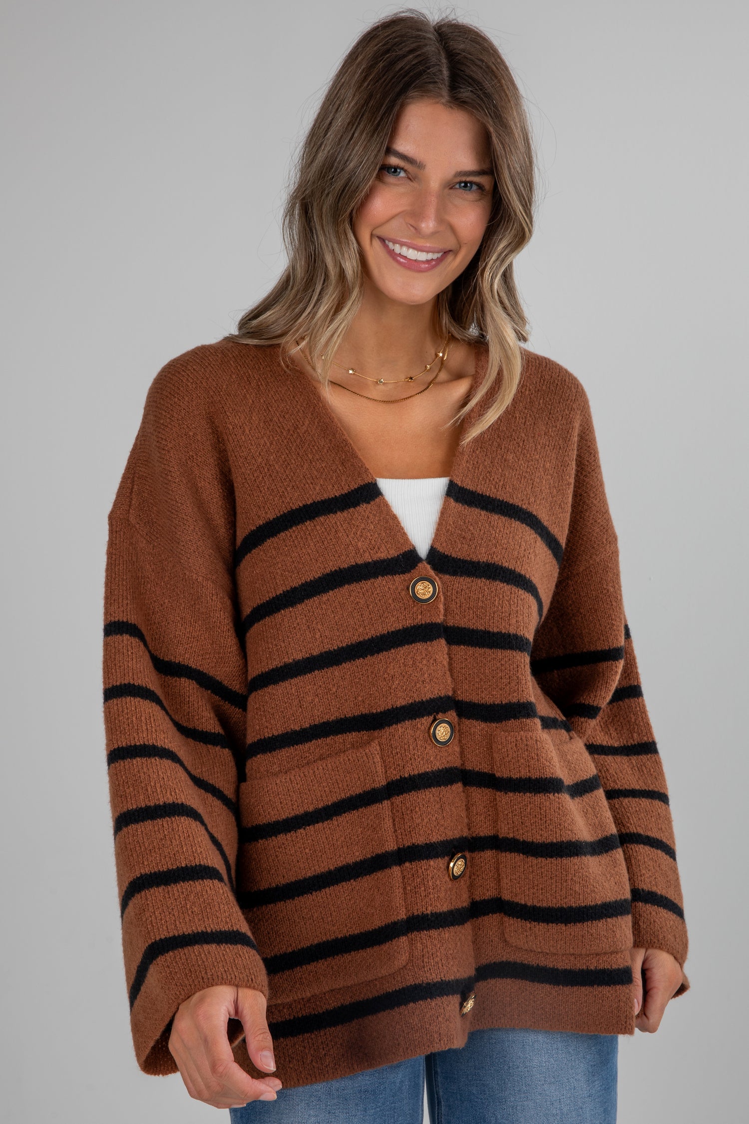 Woman wearing a brown cardigan with black stripes on a gray background