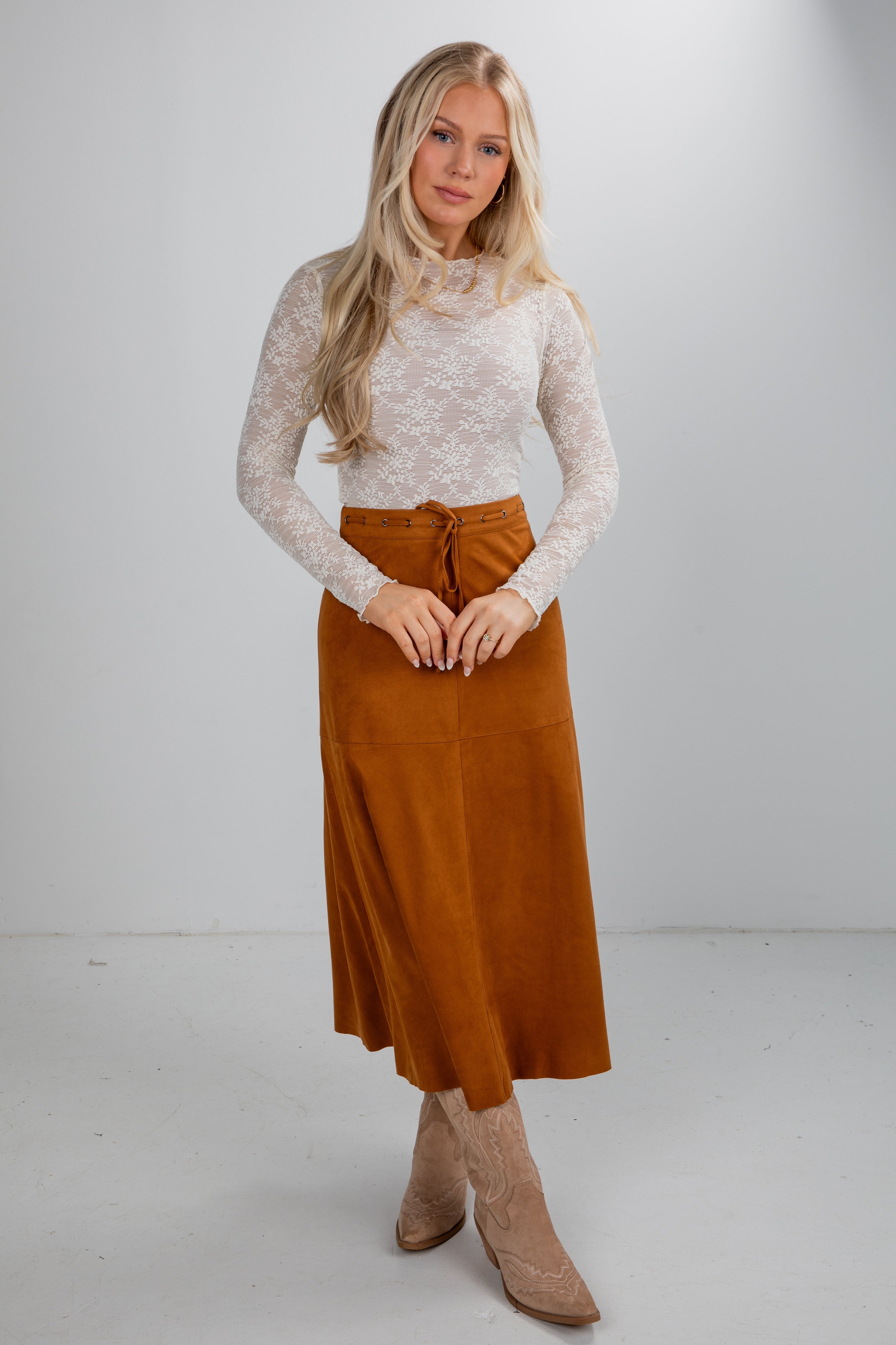 Woman wearing a white lace top and brown skirt on a plain background