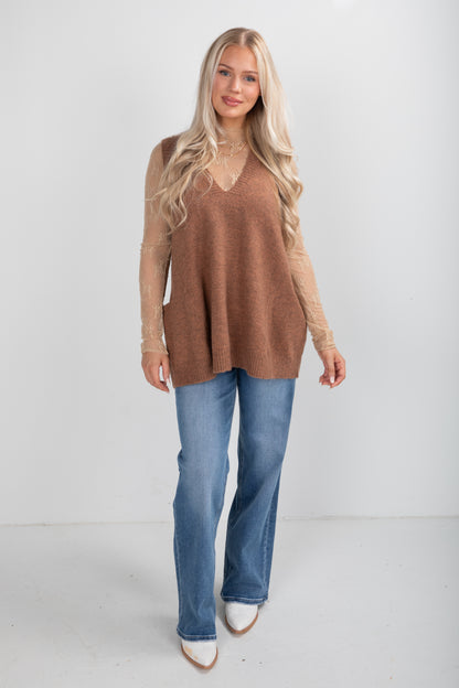 Woman wearing a brown sweater and blue jeans on a white background