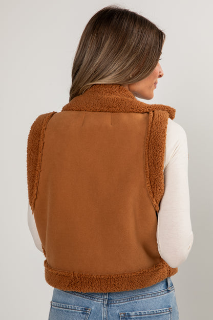 Person wearing a brown fleece vest on a plain background