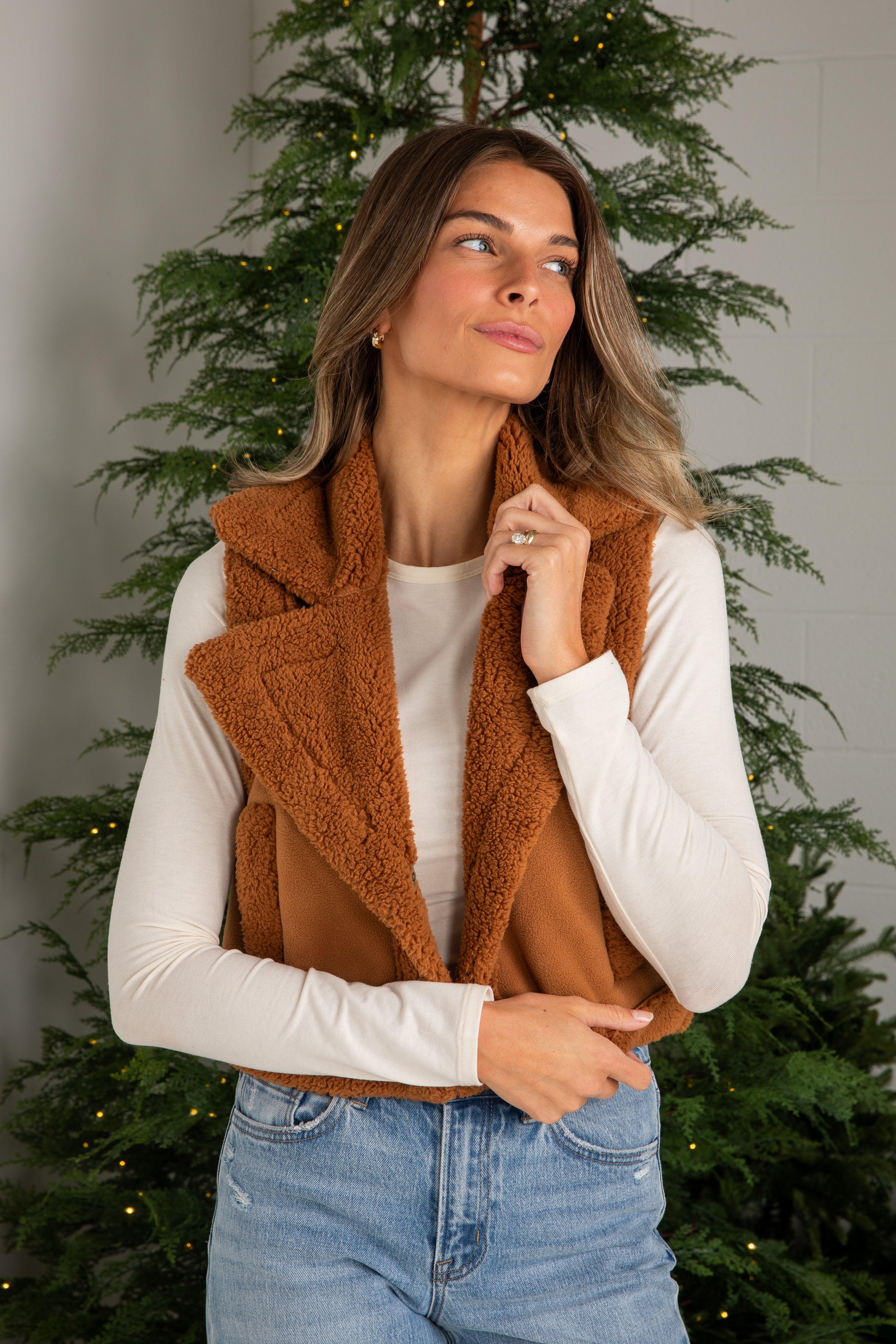 Woman wearing a brown vest over a white shirt with Christmas trees in the background