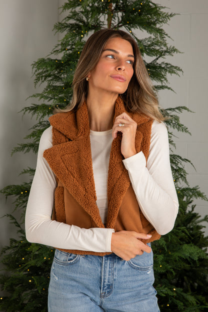Woman wearing a brown vest over a white shirt with Christmas trees in the background