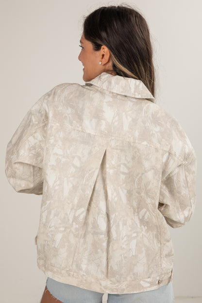 Woman wearing a light-colored floral patterned jacket against a plain background