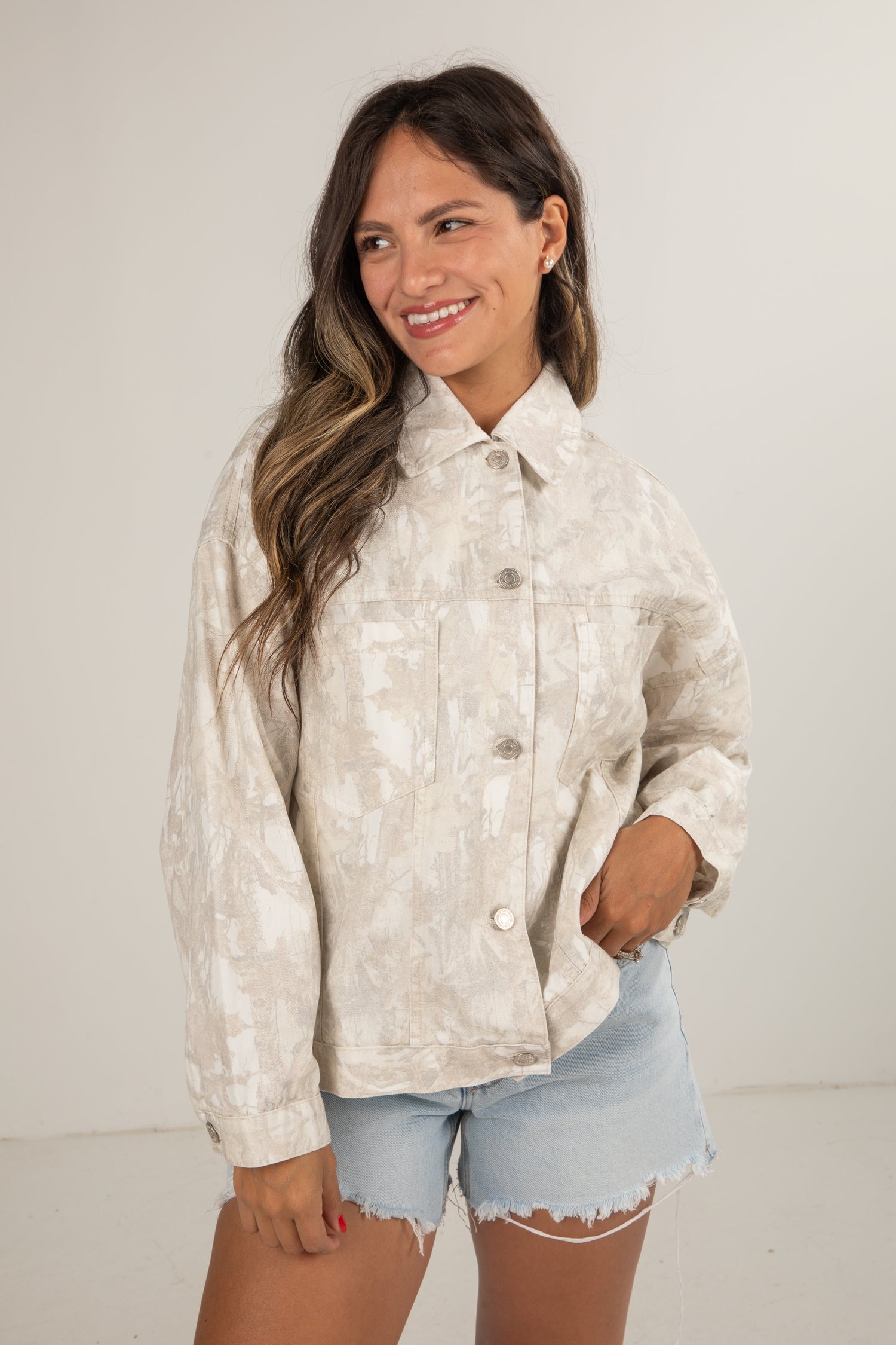 Woman wearing a light-colored patterned jacket and denim shorts against a plain background