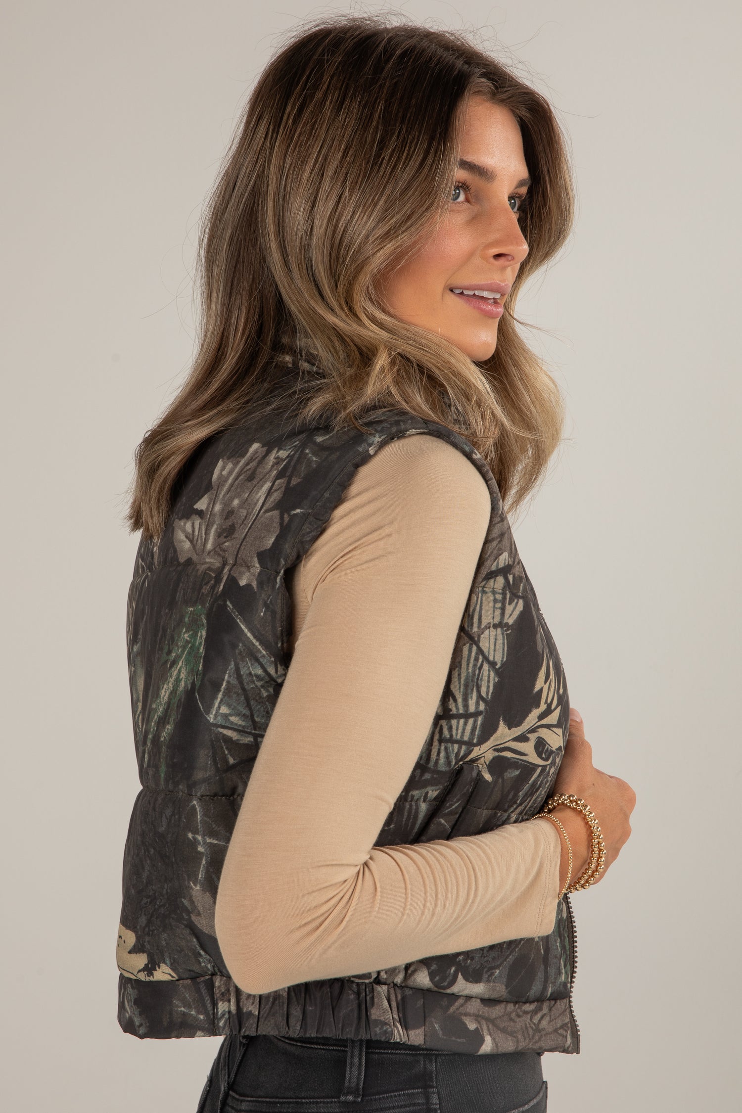 Woman wearing a camouflage vest against a plain background