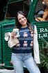 Woman in a festive sweater standing in front of a green truck with a teddy bear, holding a coffee cup.