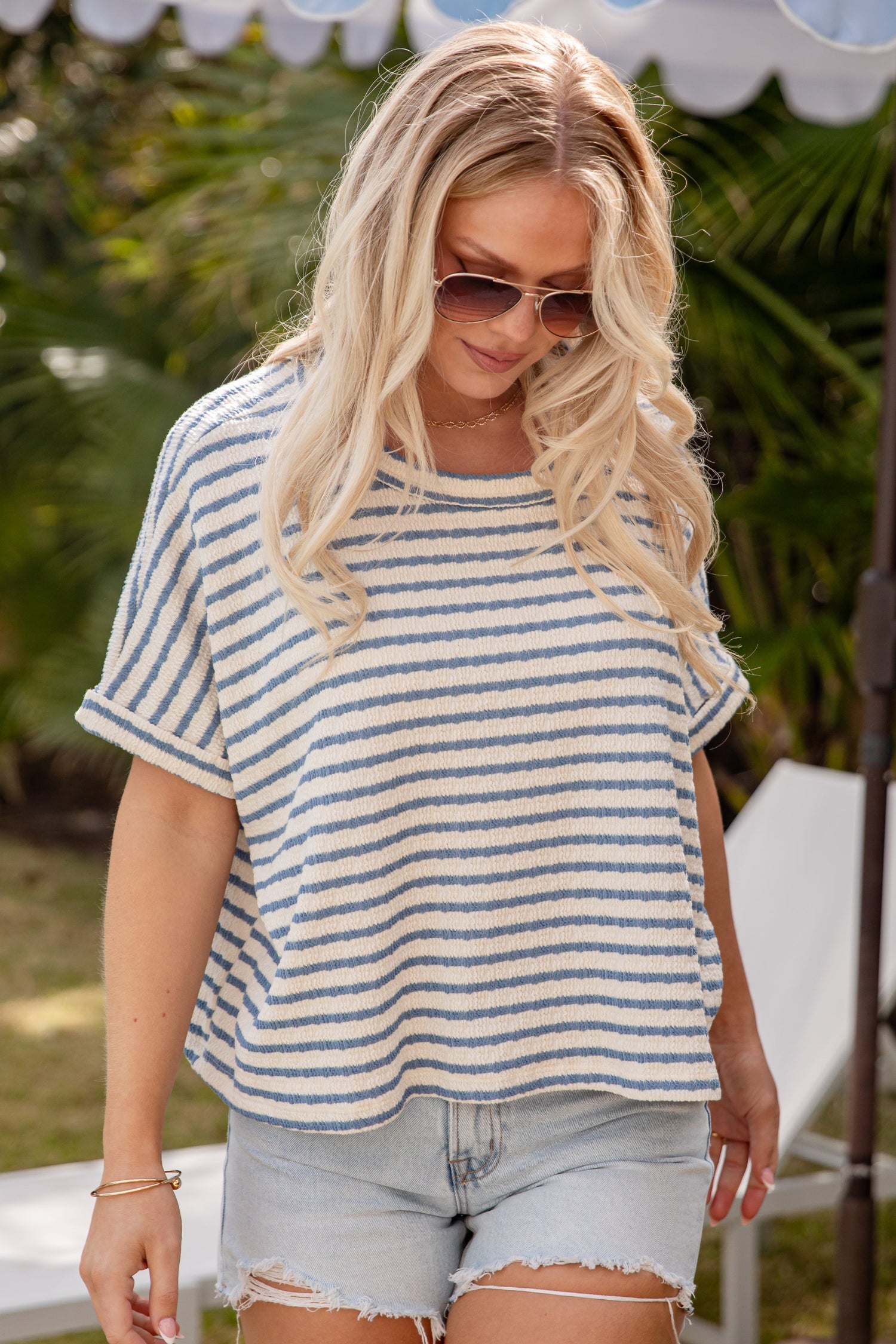 Woman wearing a striped shirt and shorts under an umbrella with greenery in the background