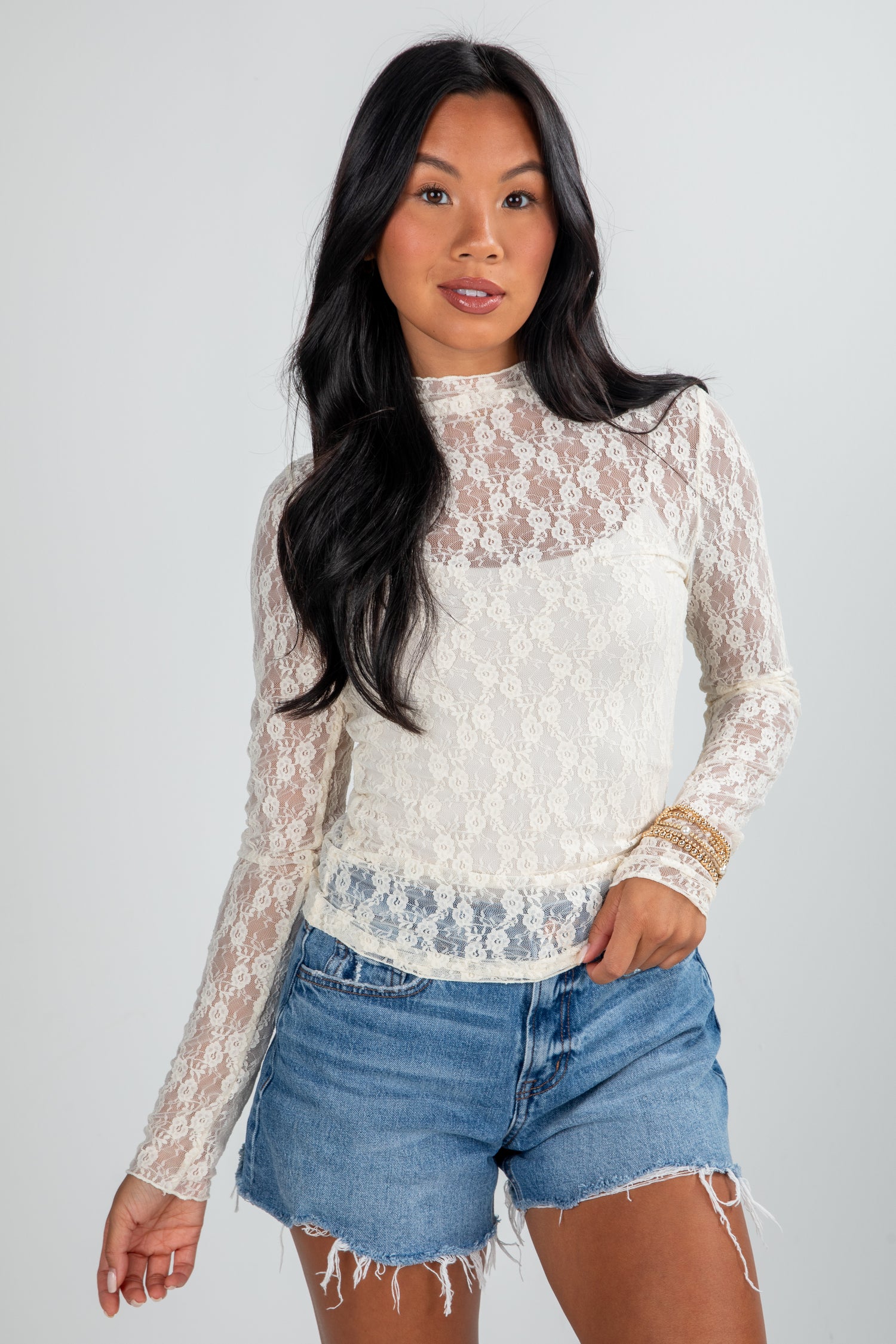 Woman wearing a lace top and denim shorts on a plain background