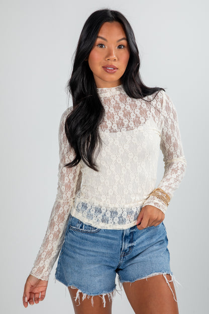 Woman wearing a lace top and denim shorts on a plain background