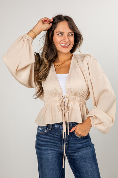Woman wearing a beige top and blue jeans against a plain background