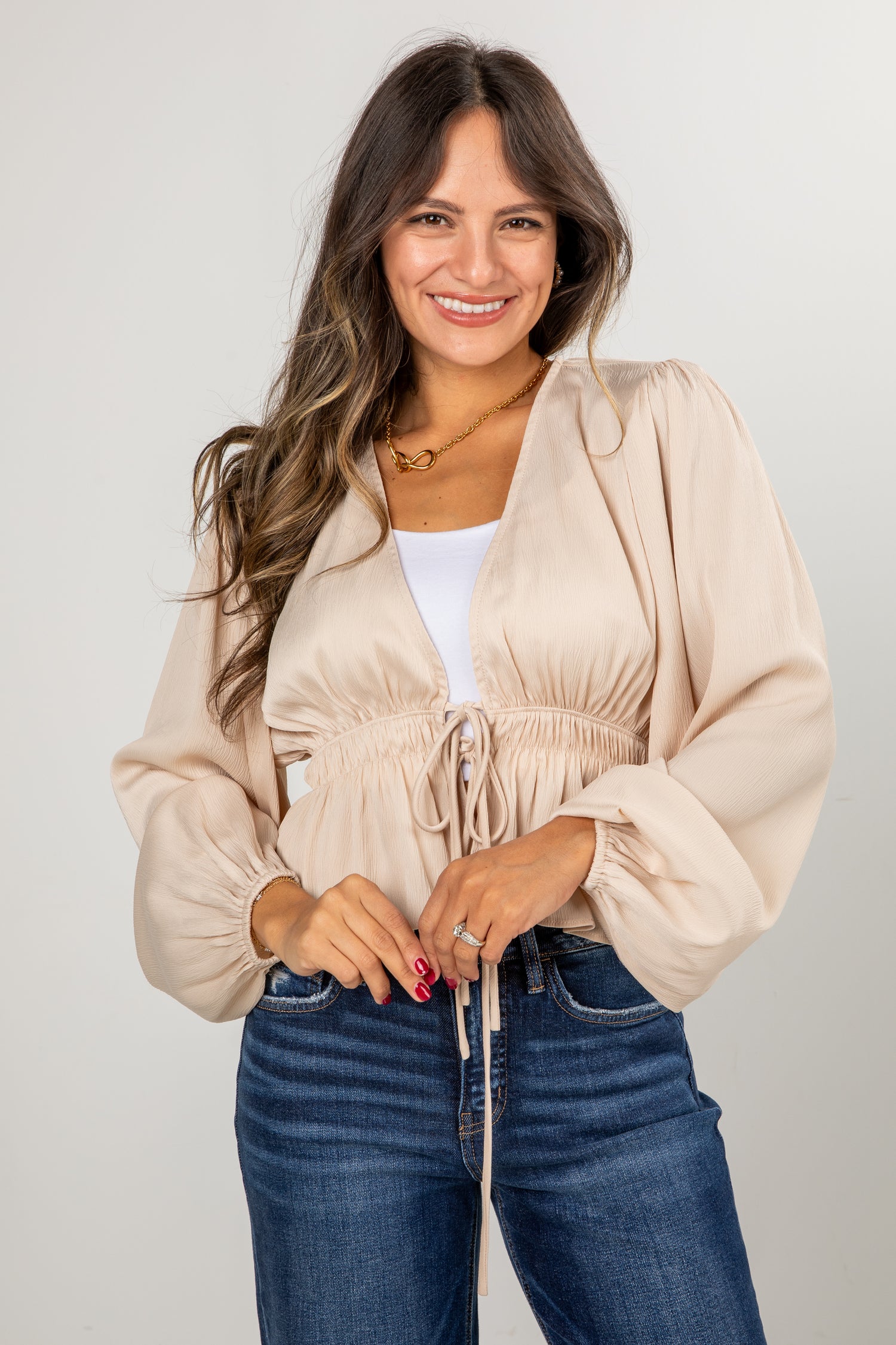 Woman wearing a beige cardigan and blue jeans against a plain background