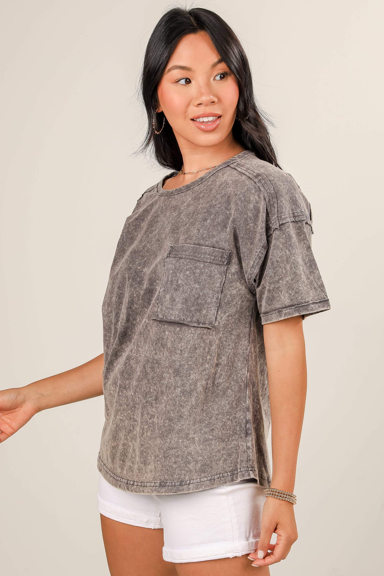 Woman wearing a gray distressed shirt with a pocket on a beige background
