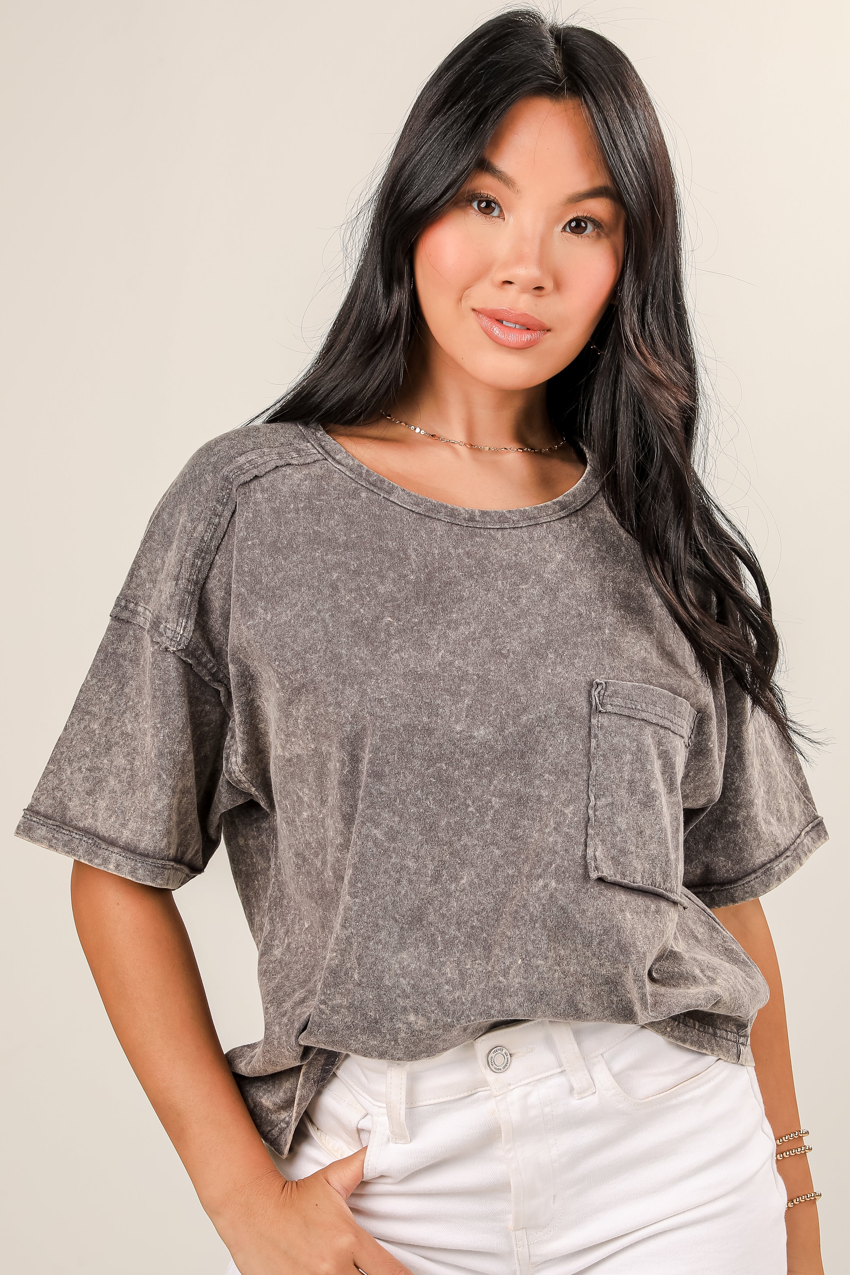Woman wearing a gray distressed shirt with rolled-up sleeves on a plain background