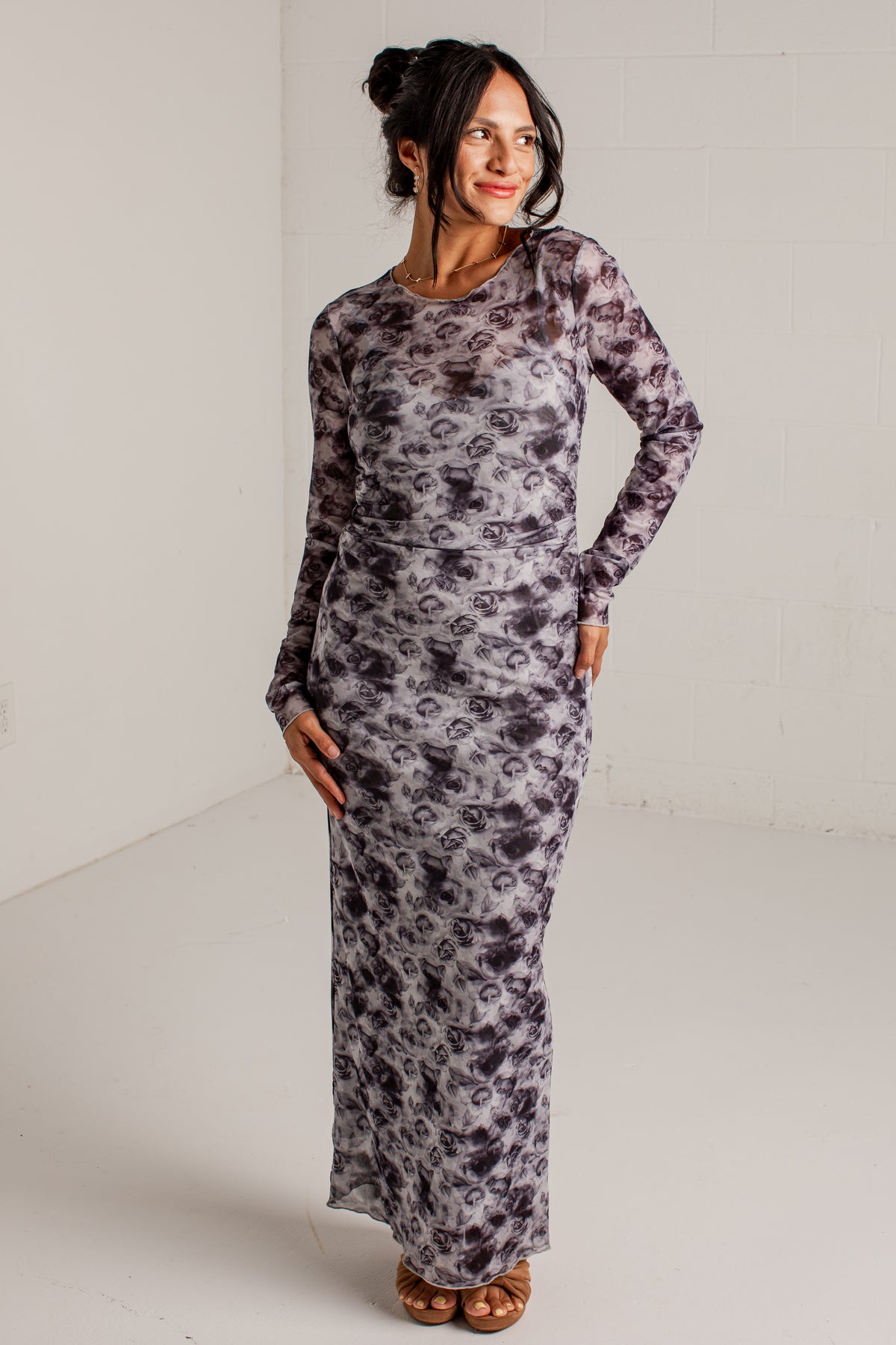 A woman modeling a long-sleeve maxi dress with a gray and white abstract tie-dye pattern, standing in a white studio setting.