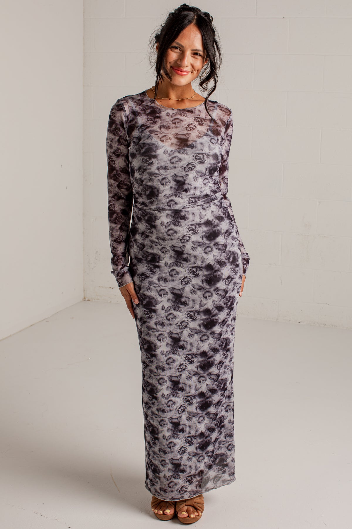 A woman modeling a long-sleeve maxi dress with a gray, black, and white abstract floral pattern, standing against a white studio wall.