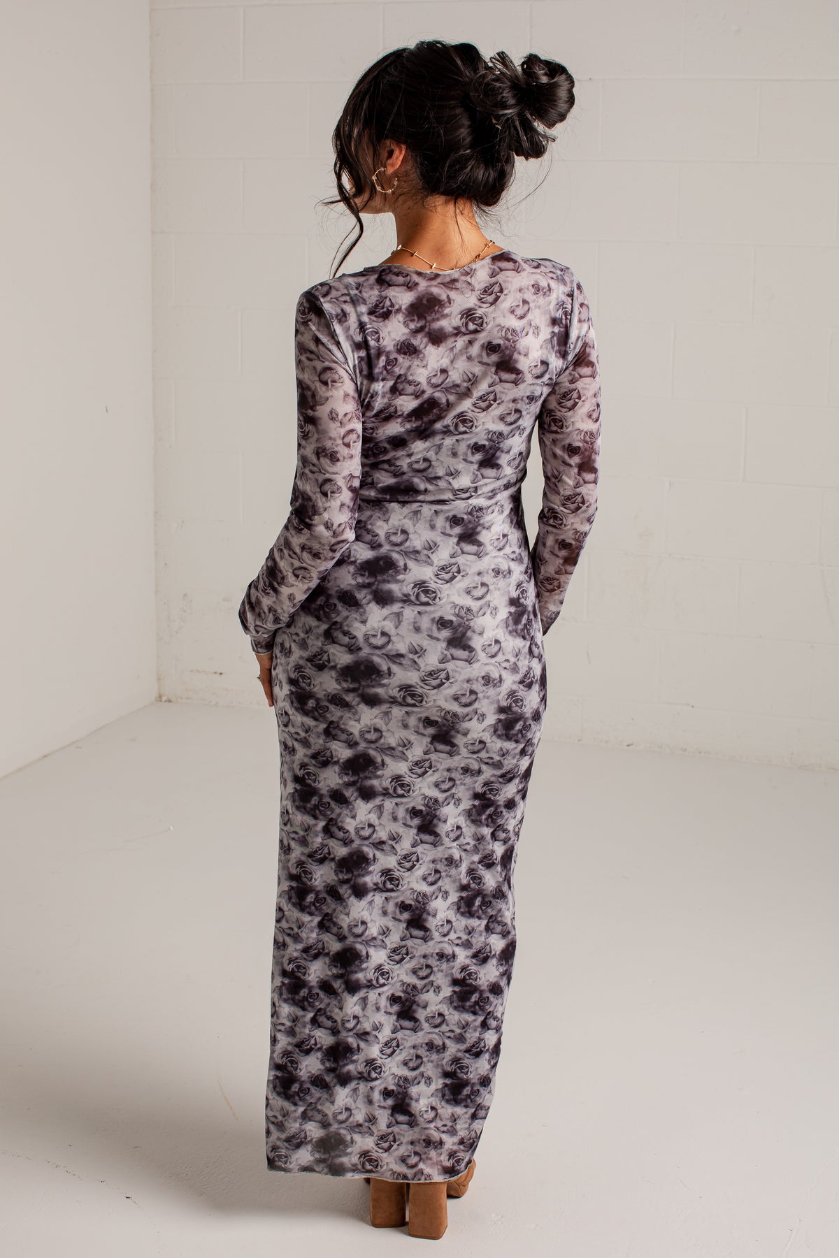 A woman viewed from behind wearing a long-sleeve maxi dress with a gray and black abstract floral pattern on a white background.