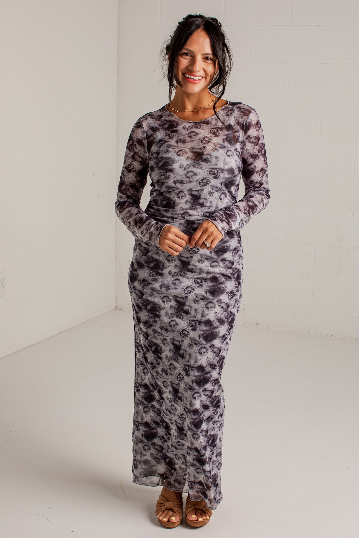 A woman modeling a long-sleeve maxi dress with a gray and black abstract floral pattern, standing against a white studio wall.