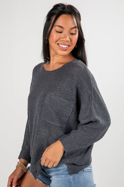 Woman wearing a dark gray sweater with a pocket on a white background