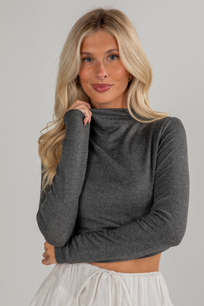 Woman wearing a gray long-sleeve top against a plain background