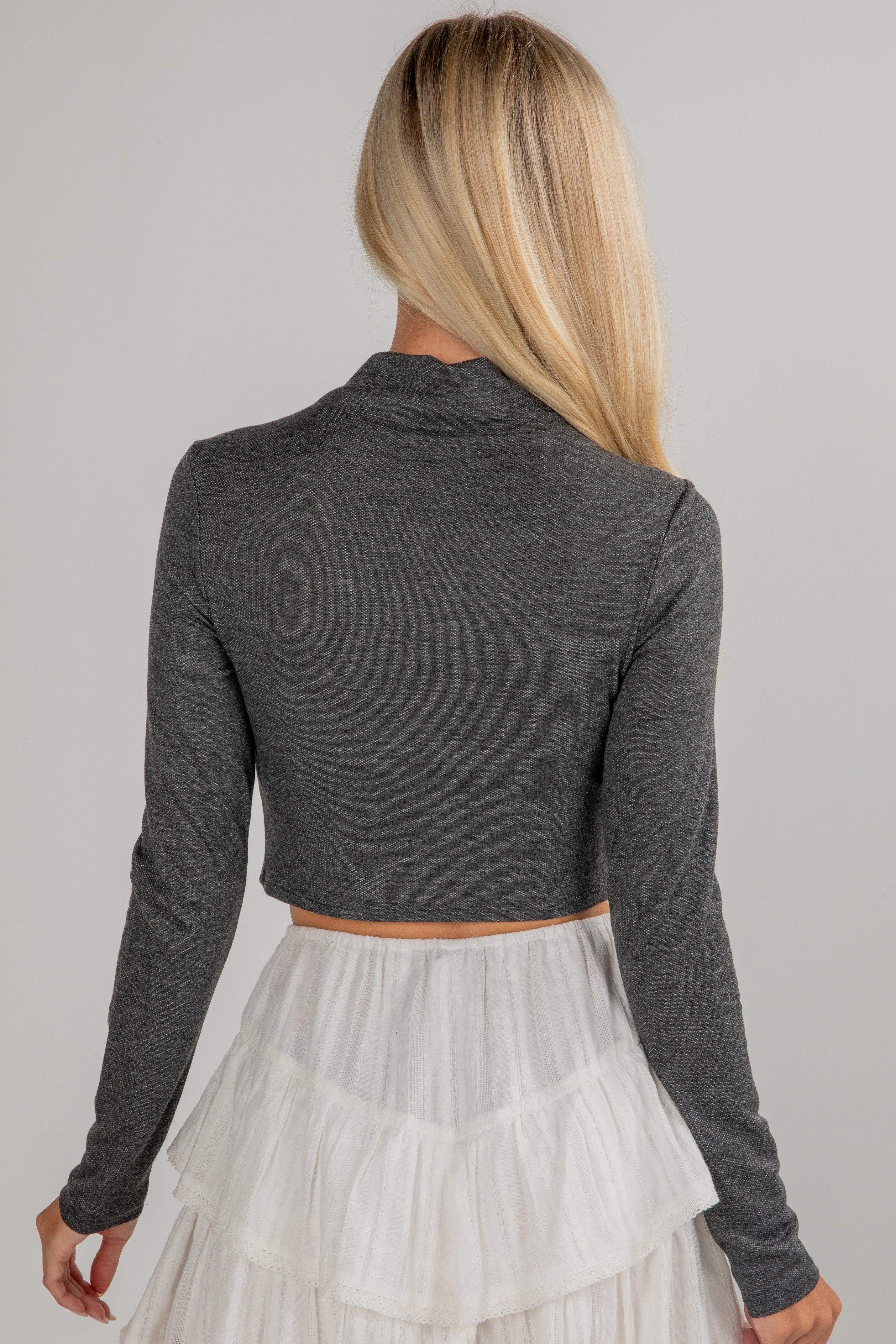 Woman wearing a gray long-sleeve crop top and white skirt on a gray background